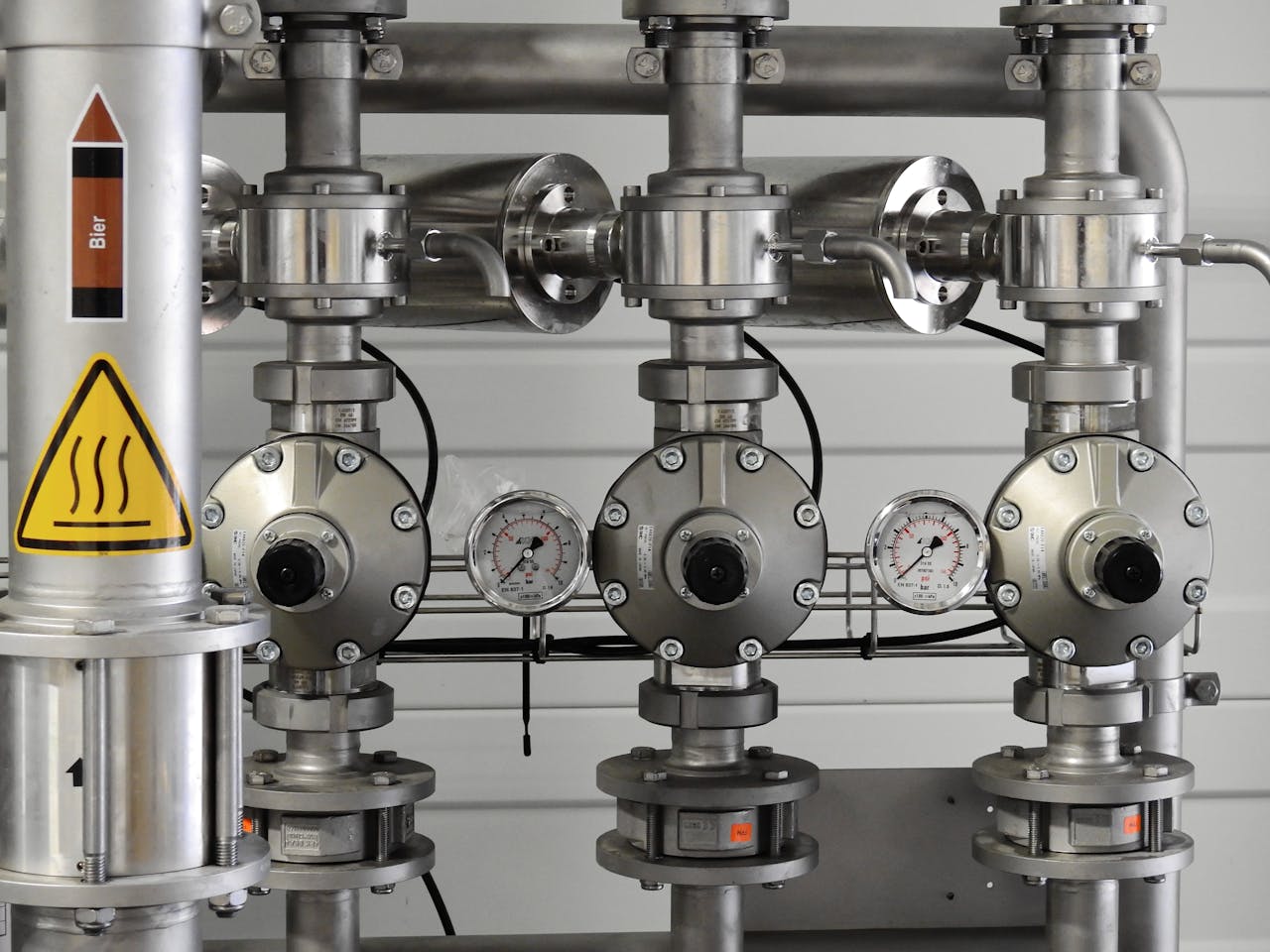 about-01 Close-up of stainless steel pipes with pressure gauges in an industrial setting.