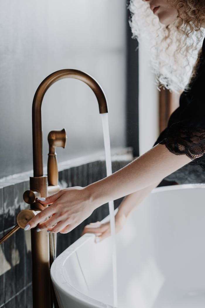 gallery-6 Elegant bathroom scene with a focus on gold faucet and female hands adjusting water flow.