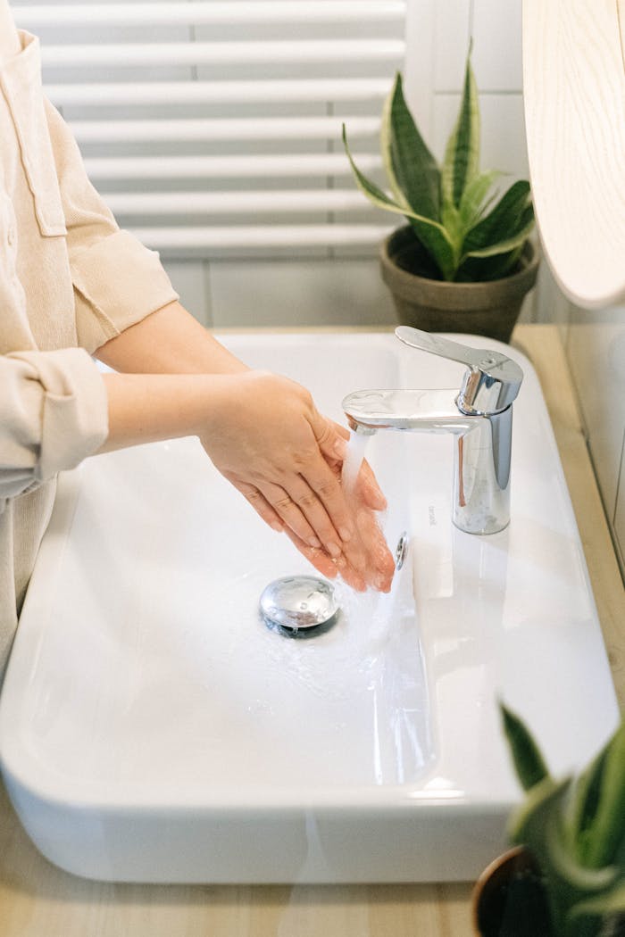 Close-up of hands being washed under a faucet with plants nearby, emphasizing hygiene.
