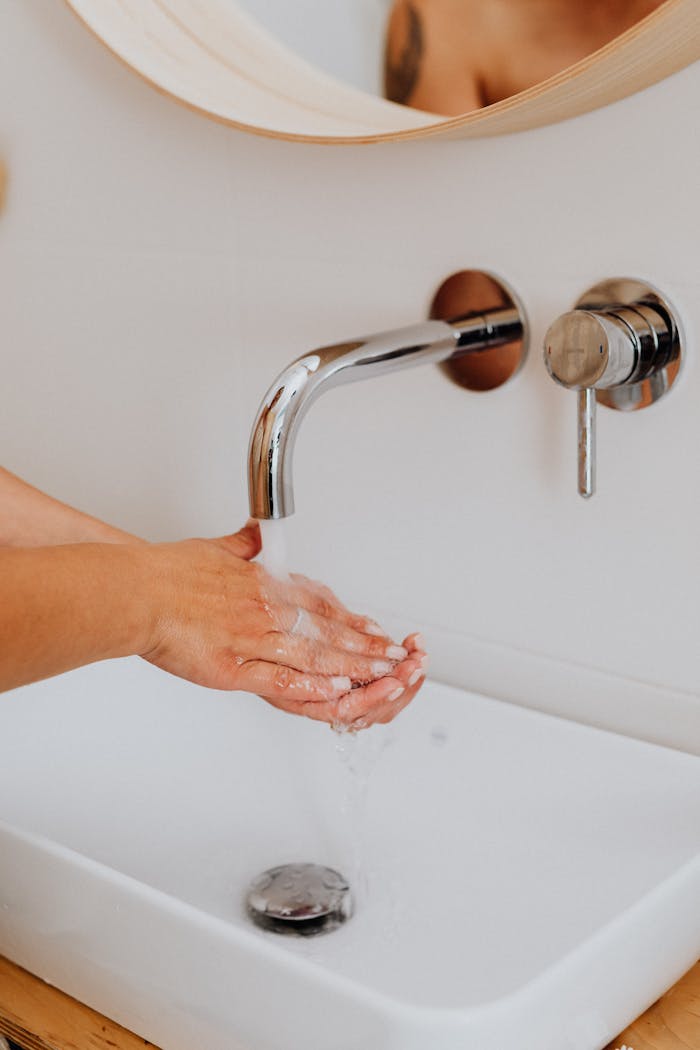gallery-3 A close-up of hands being washed in a modern bathroom with a stainless steel faucet.