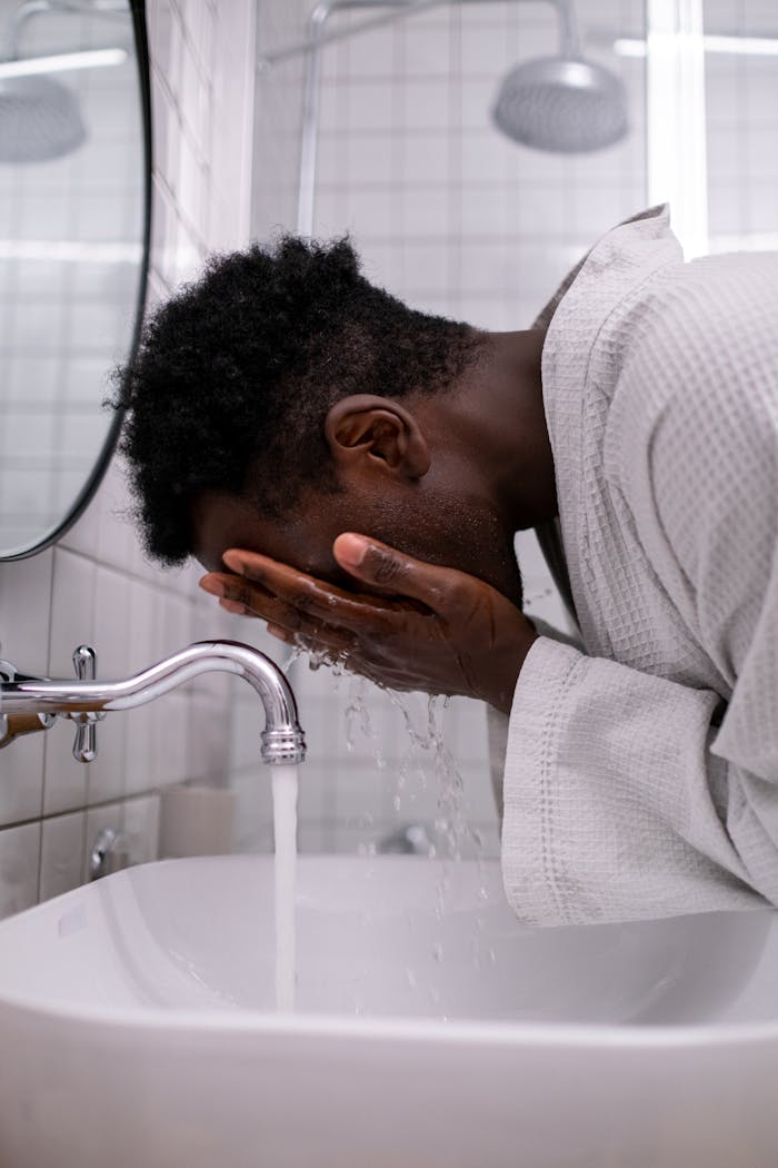 A man in a bathrobe washes his face in a modern bathroom sink.